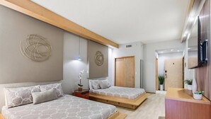 Un dormitorio moderno con dos camas, un banco de madera, una mesita y un televisor.