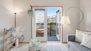 Una sala de estar con sofá, lámpara, planta, estantería y puerta que da a un balcón con piscina.