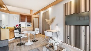 Una cocina moderna con armarios de madera, un microondas y una cafetera. Hay una zona de comedor con dos sillas blancas y una pequeña mesa.