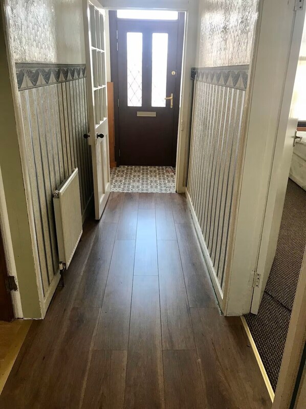 A hallway with a dark wooden floor, a patterned tile entrance, and a door with a window.