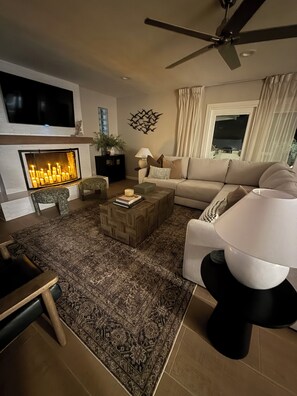 A living room with a fireplace, a ceiling fan, a sofa, a coffee table, and a TV mounted on the wall. - Go-Kart Track! 5BR Resort w/ Pool & Spa (Scottsdale)