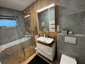 Ein modernes Badezimmer mit Duschkabine aus Glas, Holzwaschtisch und großem Spiegel.