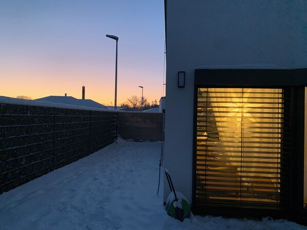 Ein verschneiter Außenbereich mit Backsteinmauer, einer Straßenlaterne und einem Gebäude mit einem Fenster mit Rollläden.