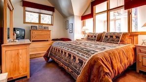 A bedroom with a large bed, wooden dresser, and a desk with a television.