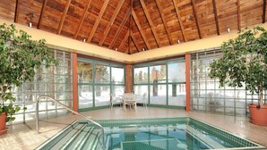 An indoor swimming pool with a wooden ceiling, glass walls, and potted plants.