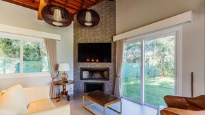 A modern living room with a stone fireplace, a flat-screen TV, and large windows offering a view of the outdoors. - Modern Apartments in Canela - DAH (Canela)
