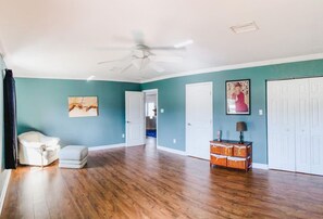 Une pièce spacieuse avec un plancher en bois, un ventilateur de plafond blanc, des murs de couleur turquoise et une porte blanche.