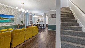 Una sala de estar moderna con un sofá amarillo, una zona de comedor y una escalera.