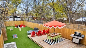 Patio con terraza de madera, una parrilla, sillas rojas, una mesa y una piscina pequeña.