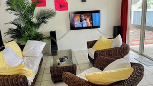 Ein Wohnzimmer mit Rattanmöbeln, einem Glastisch und einem an der Wand befestigten Fernseher.