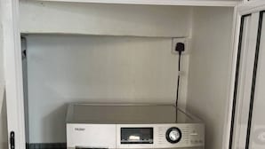 Eine kompakte, edelstahlfarbene Waschmaschine und ein Wäschetrockner in einem Gerätebaukasten, eingebaut in eine Raumecke mit Fliesenboden.