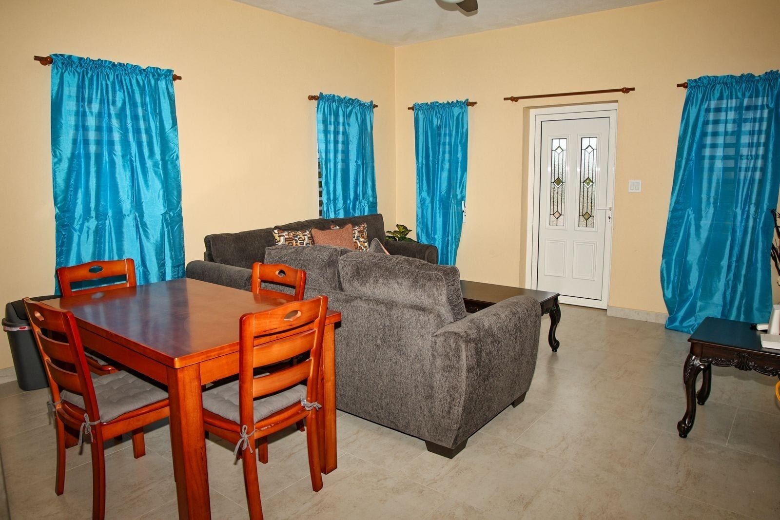A dining area with a wooden table and chairs, a gray sofa, and blue curtains.