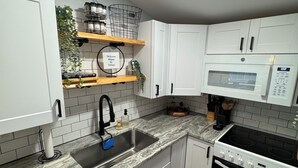 A modern kitchen with white cabinets, a stainless steel sink, a microwave, and a stove. There are shelves with kitchen utensils and a welcome sign. - Contemporary Countryside Home, Minutes to Concord (Loudon)