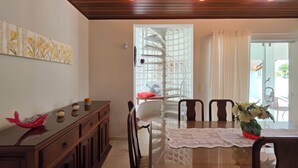Un comedor con una mesa de vidrio, sillas de madera, un cojín rojo y un jarrón de flores.
