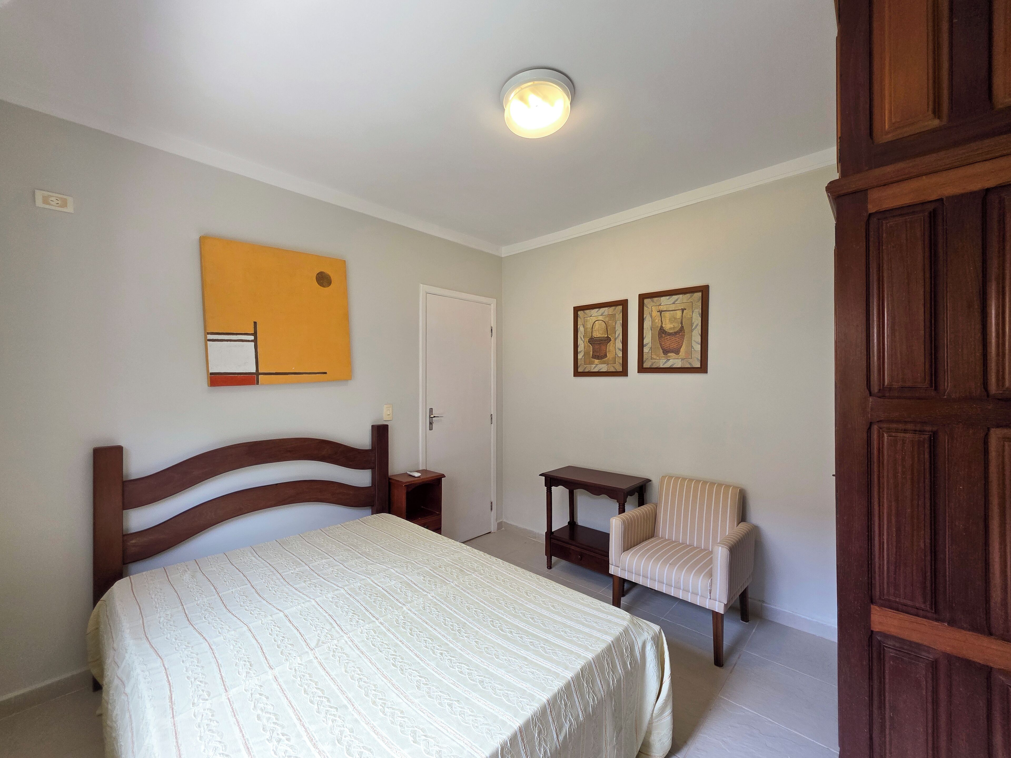 A bedroom with a bed, a chair, a small table, and two framed pictures on the wall.