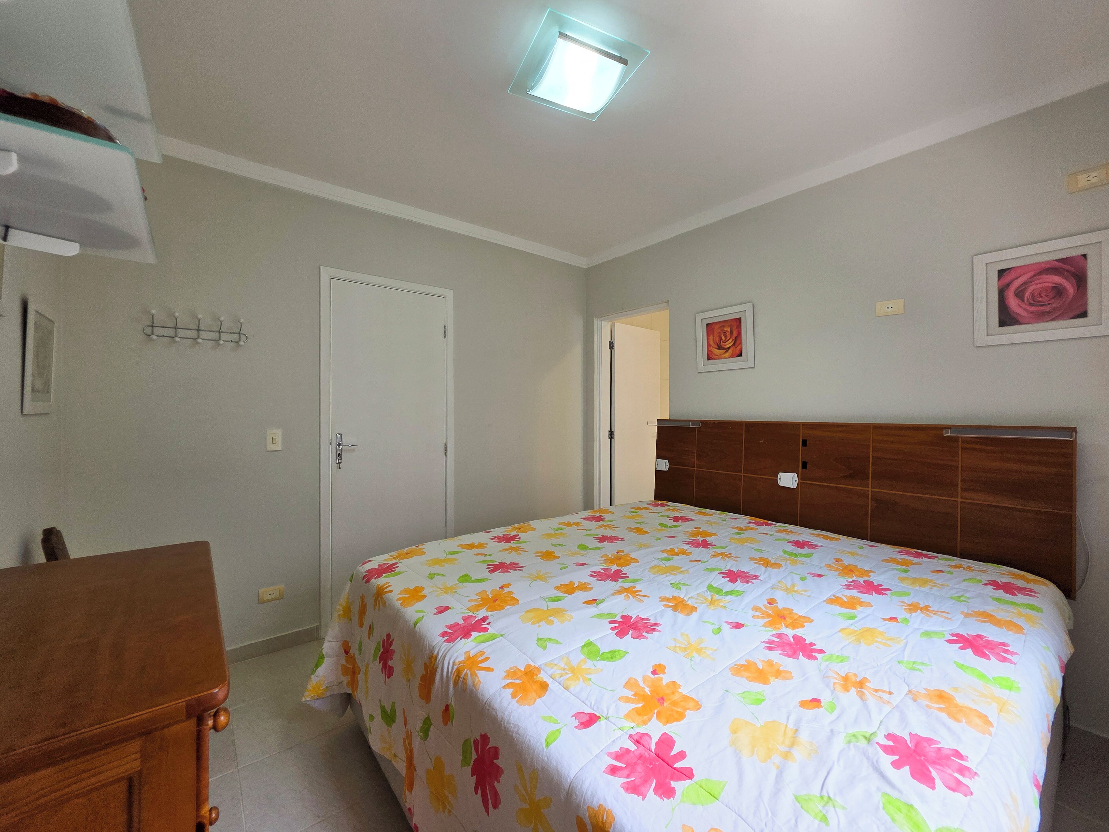 A bedroom with a floral bedspread, a wooden headboard, a white door, and a small table.