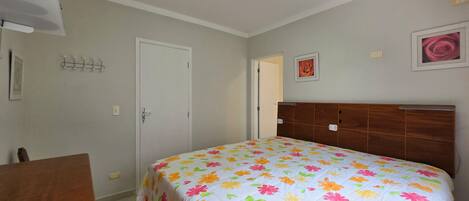 A bedroom with a floral bedspread, a wooden headboard, a white door, and a small table.