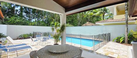 A covered outdoor area with a pool, lounge chairs, and a table.