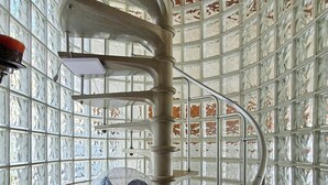 Una escalera de caracol con barandilla metálica, un banco de madera con cojín y un ventilador en la planta baja.