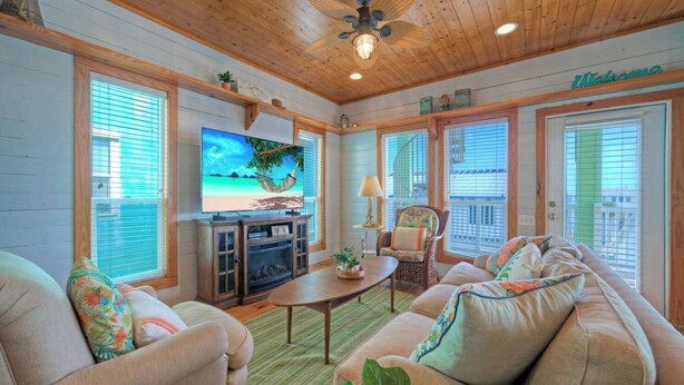 Ein gemütliches Wohnzimmer mit Fernseher, Holzboden und einer Couch mit bunten Kissen.