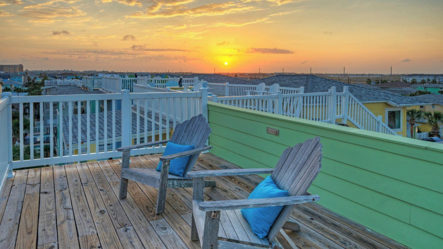 Une terrasse en bois avec deux fauteuils Adirondack, un mur végétal et une vue sur le coucher de soleil.