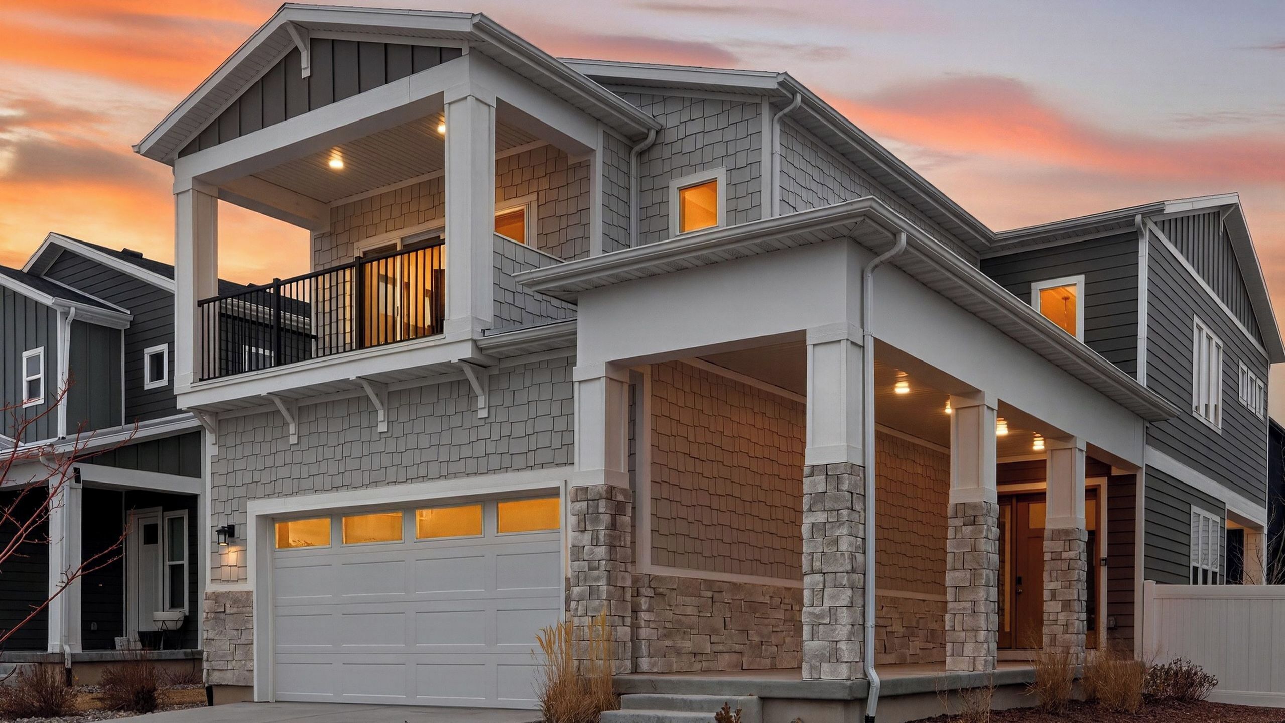 Une maison à deux étages avec un garage, un balcon et une façade en pierre.
