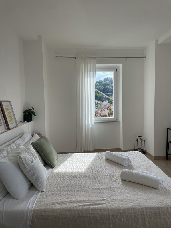 A bedroom with a large bed, white curtains, a view of a landscape, and a small table with a lamp. - Bed&BikeItalia Anguillara Sabazia II Sogno del Lago (Anguillara Sabazia)