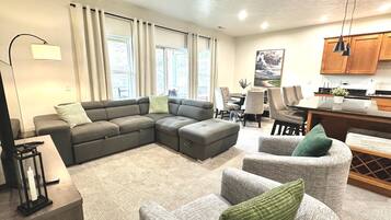 A modern living room with a sectional sofa, two armchairs, a dining area, and a kitchen.