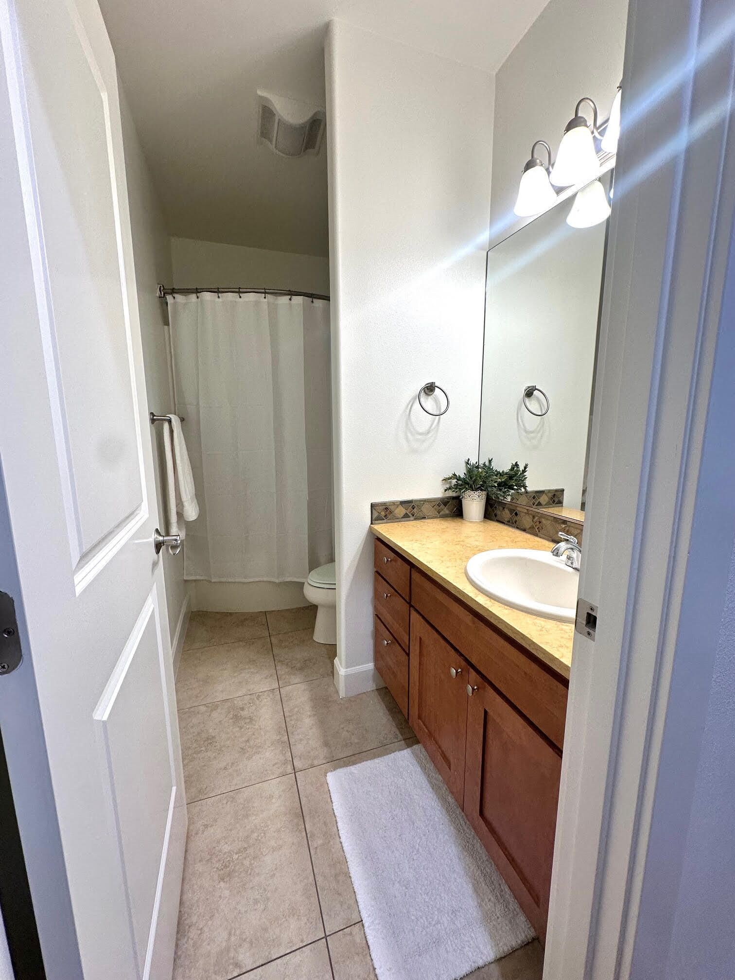 Een badkamer met een wit toilet, een douchegordijn, een wastafel met spiegel en een handdoekhouder.