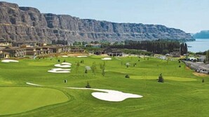 Un parcours de golf doté de bunkers, d’un club-house et offrant une vue sur un paysage montagneux.