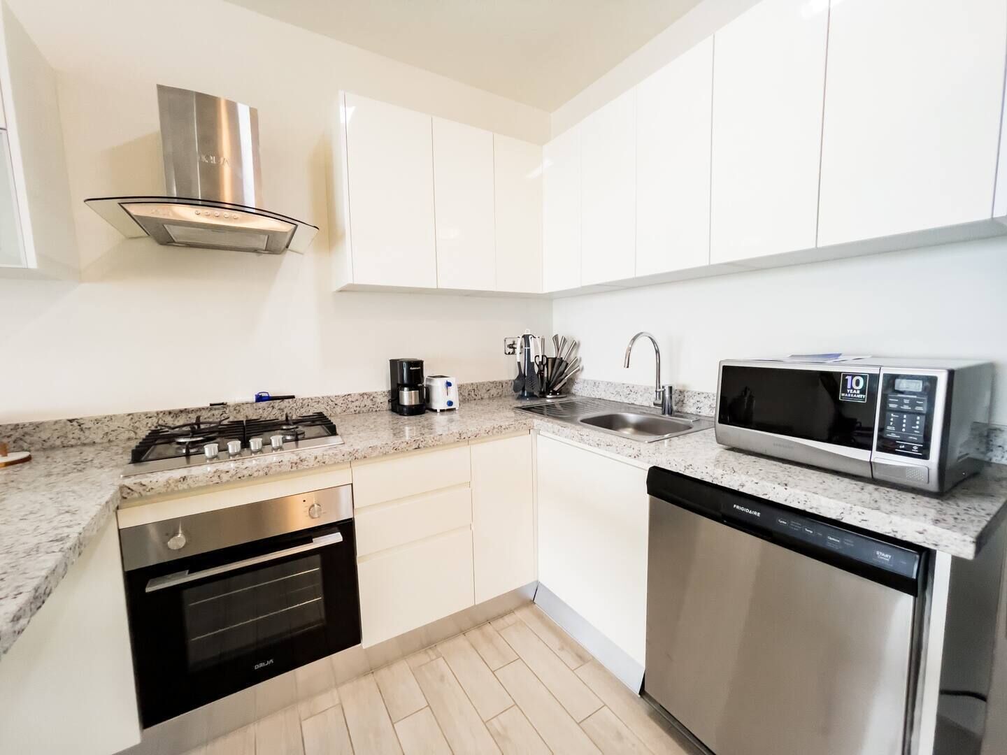 Een moderne keuken met witte kastjes, een roestvrijstalen fornuis, een vaatwasser en een magnetron.