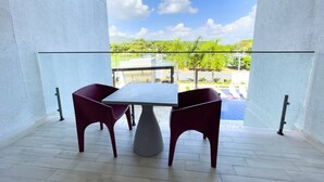 Un balcón con mesa y sillas, que ofrece vistas a una piscina y vegetación.