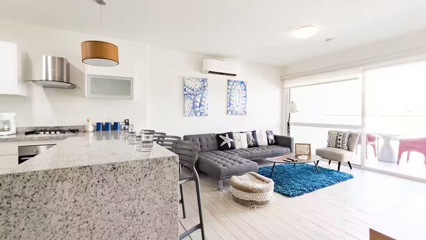 Una cocina moderna con encimera de granito, un sofá gris y una alfombra azul.