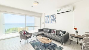 A modern living room with a grey sectional sofa, a coffee table, and a view of the sea through large windows. - Sanctuary Reef -S2-507- 2 bed, 2 bath (Punta Chame)