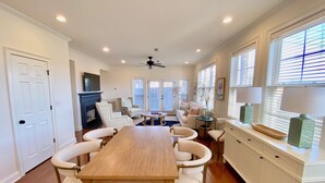 A spacious dining area with a long wooden table and white chairs, a fireplace, and a ceiling fan. - Reedy River Retreat - Walk to Everything Downtown (Greenville)