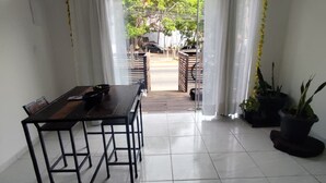 A spacious room with a large dining table, a view through a glass door to an outdoor area with a car and greenery. - KITNET MEU SONHO BUZIOS (Buzios)