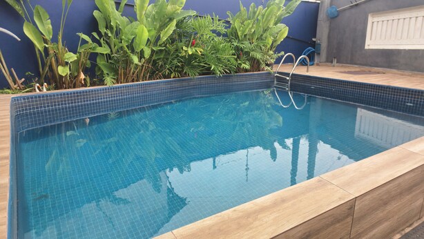 Piscina rectangular amb vora de rajola, envoltada de plantes i un pont de fusta.