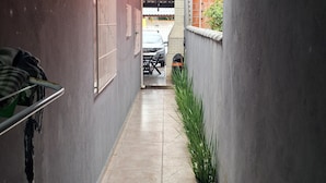 Passadís estret i emblanquinat, amb un portal metàl·lic a l'esquerra, una petita planta a la dreta i un cotxe visible a través del portal.