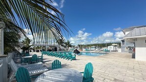 A poolside area with turquoise chairs and tables, a pool, and a view of the surrounding buildings. - Cozy Trailer Retreat - Key Largo (key largo)