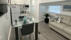 A modern kitchen with white cabinets, a glass dining table, and a beige sofa. - Cozy Trailer Retreat - Key Largo (key largo)