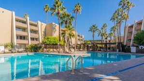 A swimming pool with lounge chairs and palm trees, surrounded by multi-story buildings. - New Listing with Premier Host Luxury Meets Comfort Walk to Old Town Heated Pool (SCOTTSDALE)