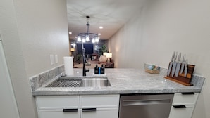 A kitchen with a granite countertop, stainless steel sink, and white cabinetry. There is a dish rack, a set of knives, and a basket of magazines on the counter. - New Listing with Premier Host Luxury Meets Comfort Walk to Old Town Heated Pool (SCOTTSDALE)