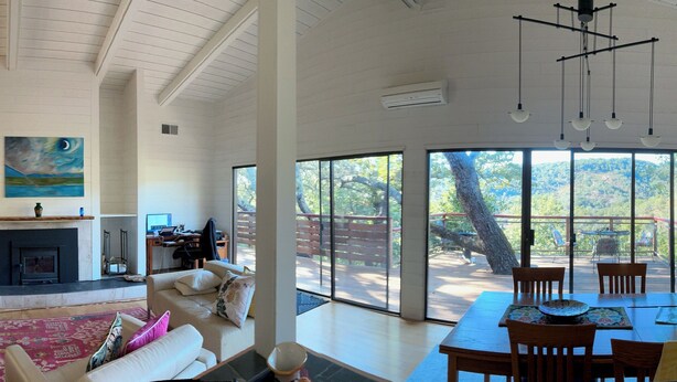 Uma sala de estar ampla com lareira, um espaço para refeições com vista e uma grande janela com vista para um deck.