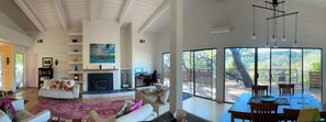 Amplia sala de estar con chimenea, comedor con vistas y un gran ventanal con vista a una terraza.