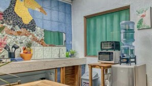 Een kleine keuken met een houten tafel, een magnetron, een waterdispenser en een koelkast.