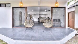 Ein modernes Haus mit einer großen Glasdoor, die zu einem Essbereich mit zwei Korbstühlen und einer Küche im Hintergrund führt.