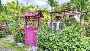 Ein tropisches Resort mit einem rosafarbenen Tor, auf dem 'Tres Pipas Beach House Bungalows' steht.