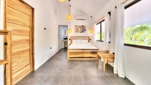 Ein modernes Schlafzimmer mit einem hölzernen Bett, einer kleinen Holzbank und einem großen Fenster mit Blick auf Grünflächen.
