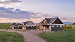A row of three single-story houses with attached garages, set in a rural landscape with a gravel driveway leading to the entrance. - New! Modern Retreat, Fireplace, Mountain Views, Hike, Fish, Bozeman, Yellowstone (Bozeman)