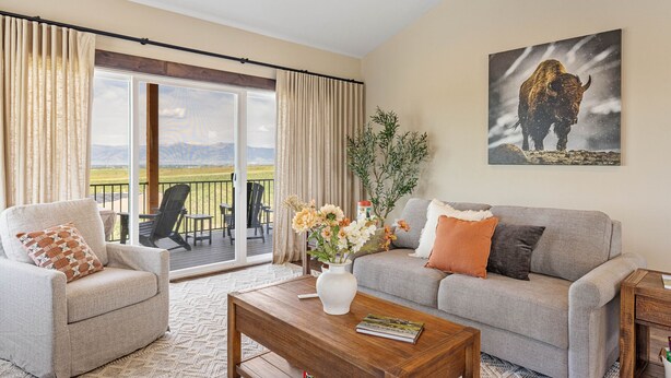 A living room with a sofa, armchair, and coffee table, a painting of a bison, and a view of mountains through large sliding doors. - New! Modern Retreat, Fireplace, Mountain Views, Hike, Fish, Bozeman, Yellowstone (Bozeman)